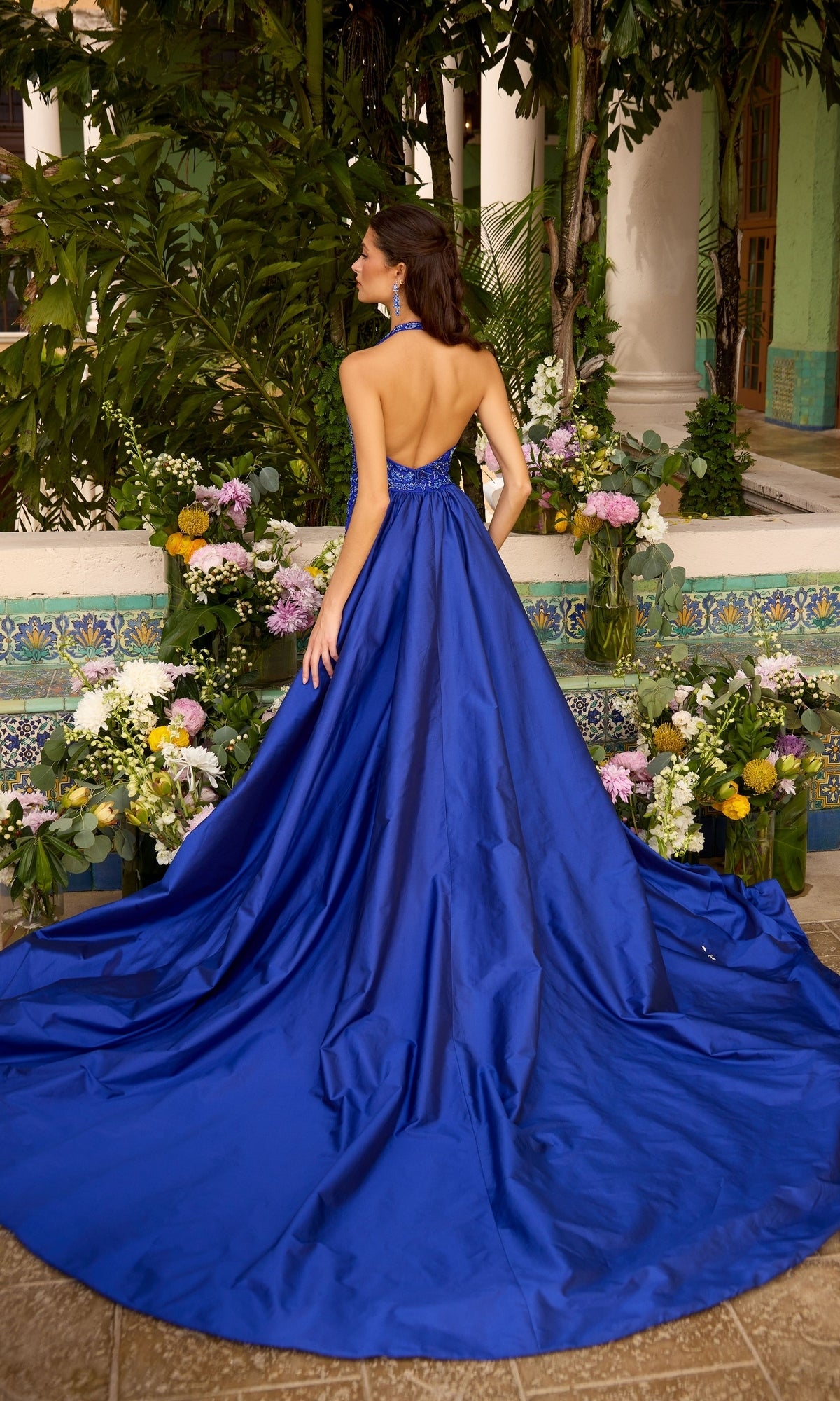 Back view of a woman wearing an Ava Presley 47421, an open-back, royal blue, sleeveless floor-length gown with a full skirt and train.